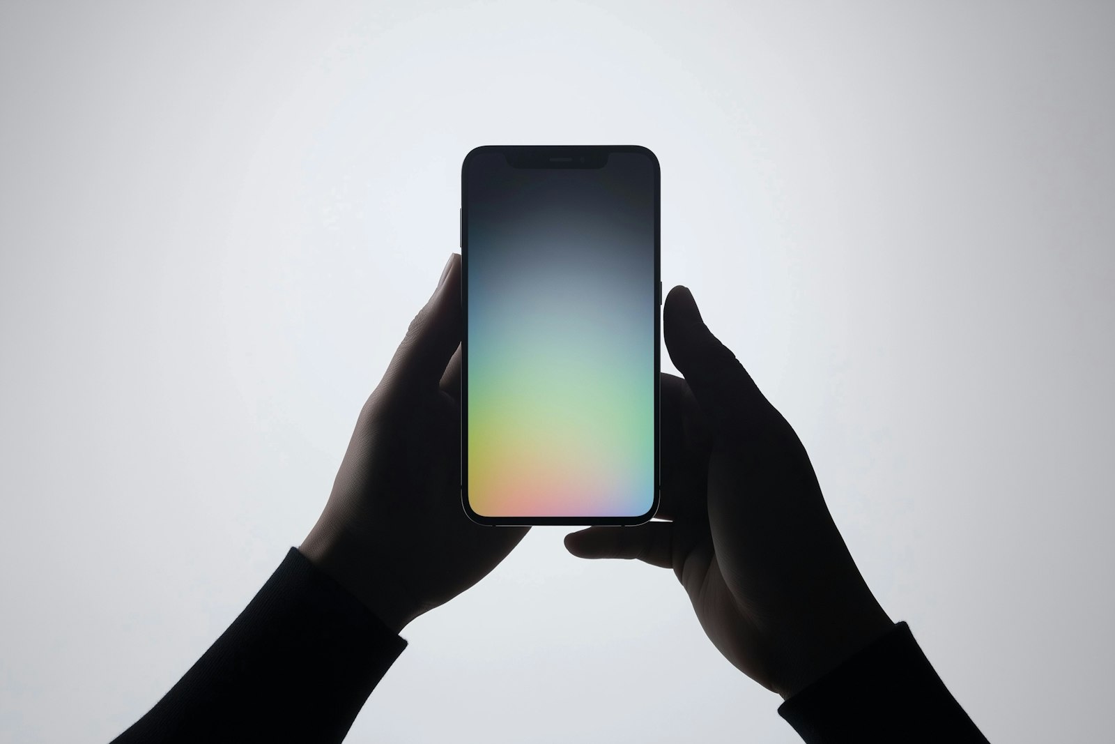 Hands holding a smartphone with a soft gradient on its screen against a pale grey background